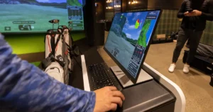 A golfer checks shot data on an X-Golf simulator to improve performance.