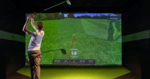 Person swinging a golf club in front of a golf simulator screen, demonstrating golf rules for beginners with realistic visuals and shot tracking data