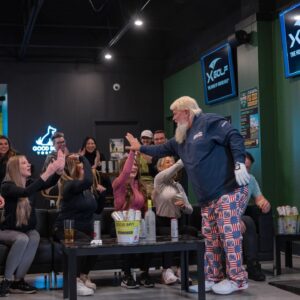man wearing one golf glove. He is at X-Golf Rockwall indoor event space for golf simulators. He is wearing funky pants and cheering with the crowd.