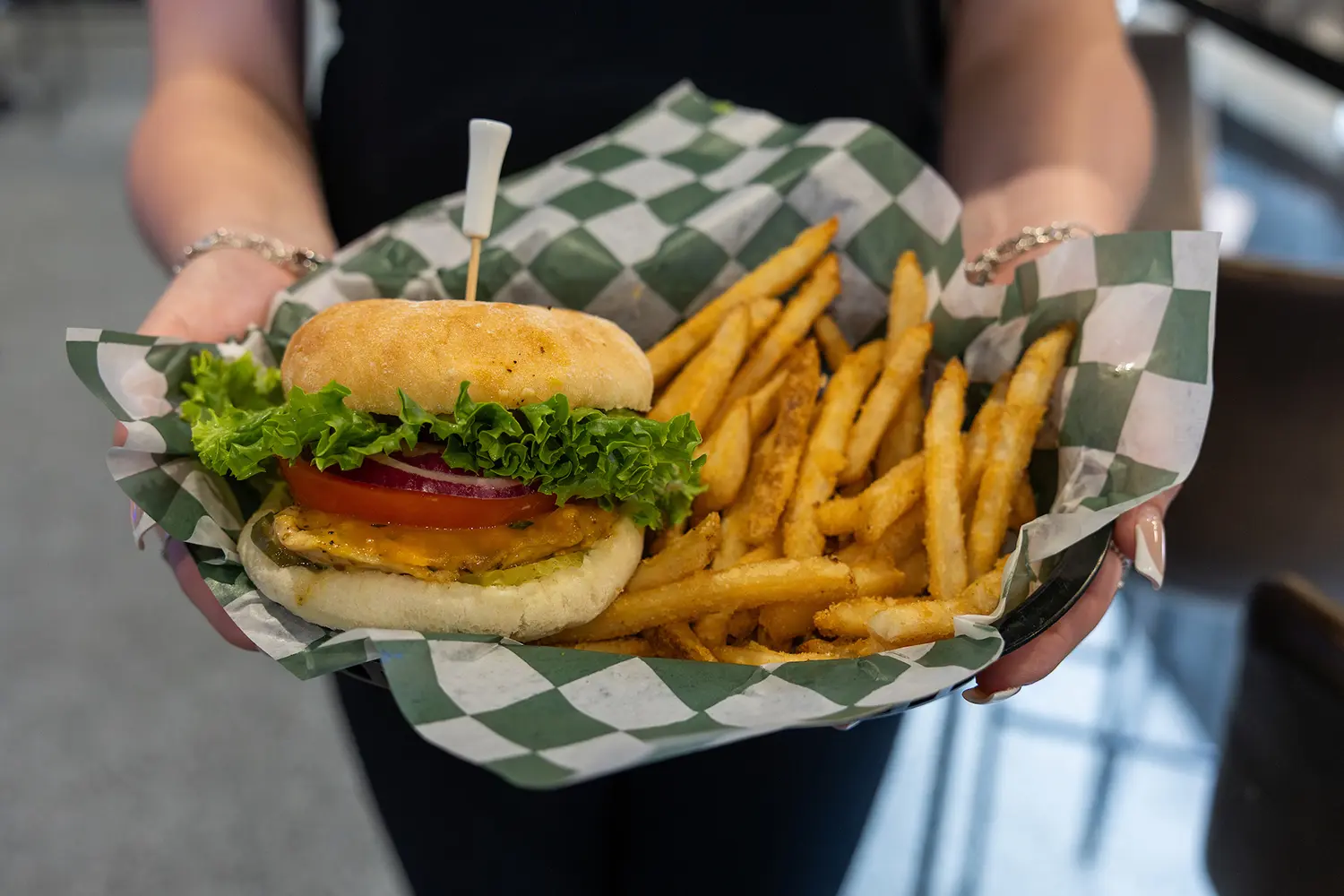 Grilled chicken sandwich with lettuce, tomato, and fries in a basket lined with checkered paper.