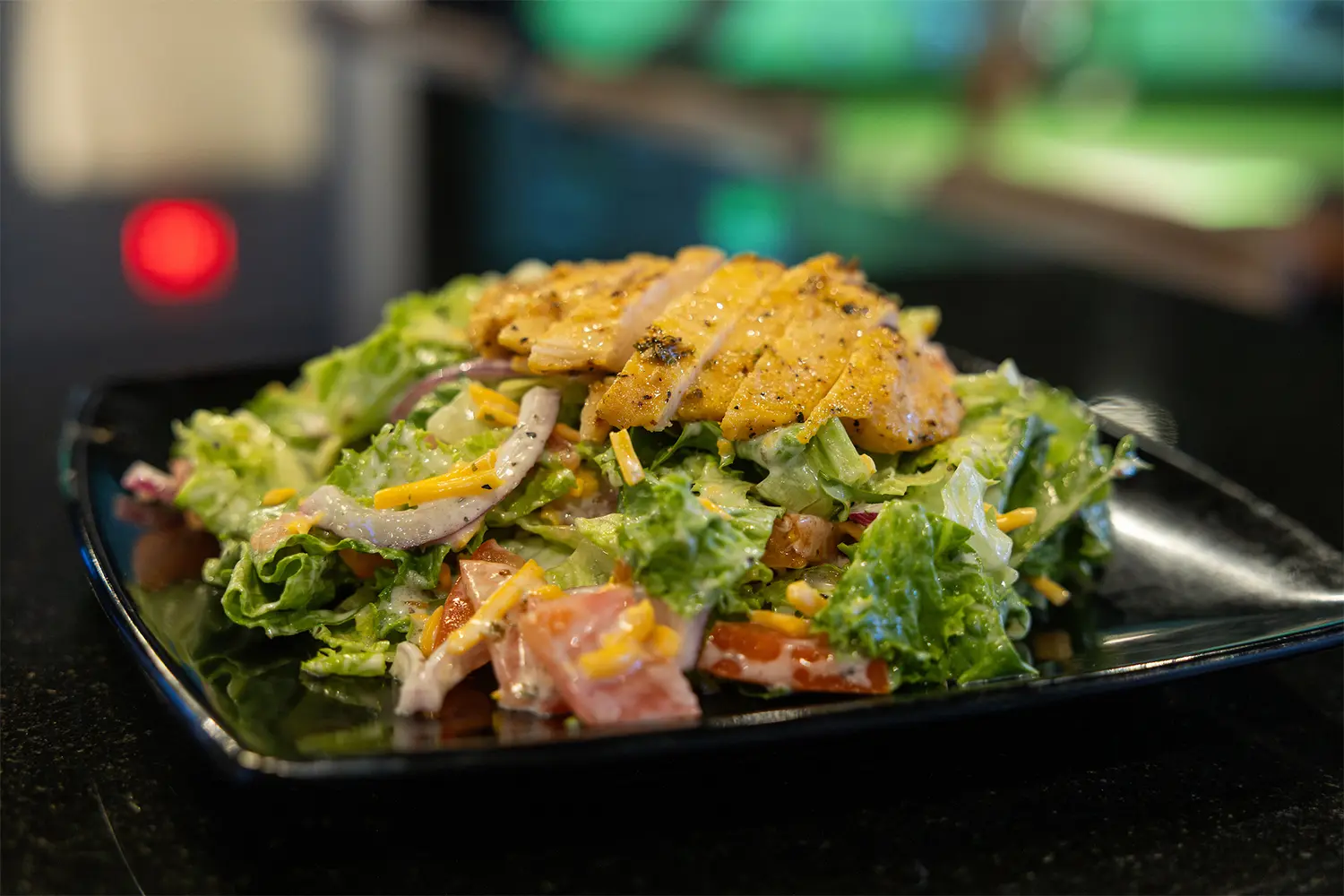 Close-up of a fresh salad topped with grilled chicken strips, shredded cheese, and onions.