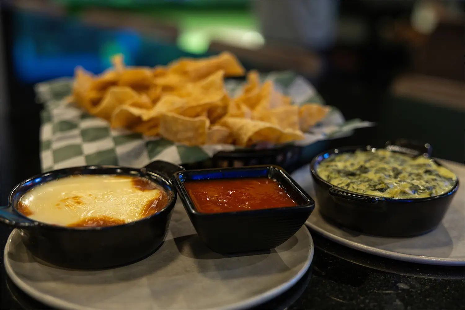 Trio of dips including queso, salsa, and spinach artichoke dip with a basket of tortilla chips.