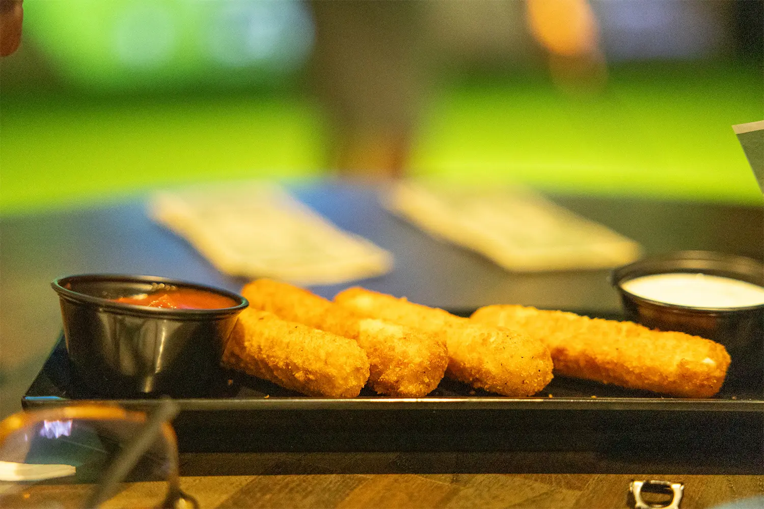 Fried mozzarella sticks served with marinara and ranch dipping sauces on a rectangular plate.