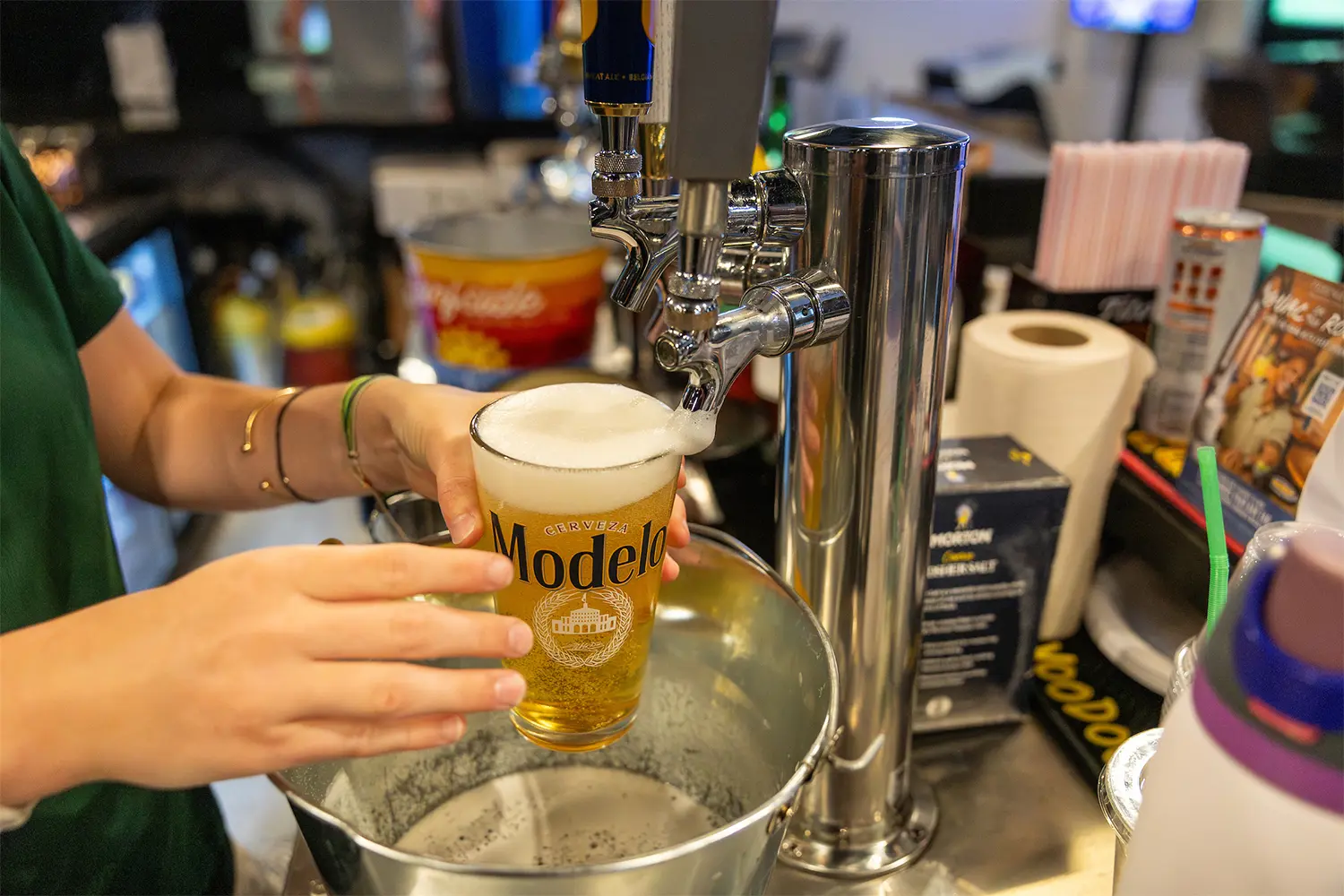 Bartender pouring a draft Modelo beer into a chilled pint glass at the bar.