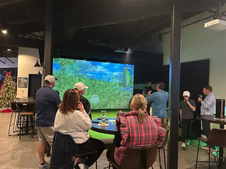 Groups gather around simulators during holiday league night with a Christmas tree visible in the background.