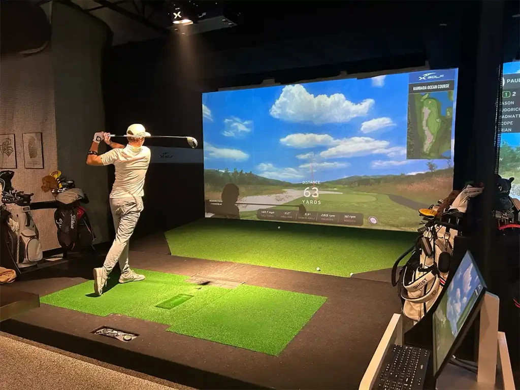 Golfer completes his swing as the simulator tracks a 63-yard approach shot with ball speed and spin data displayed.